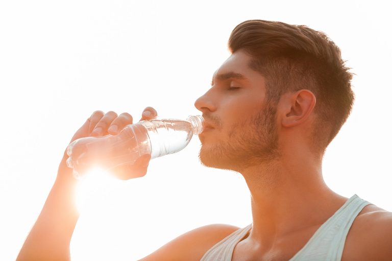 Staying hydrated. Low angle view of young man drinking water and keeping eyes closed while standing outdoors